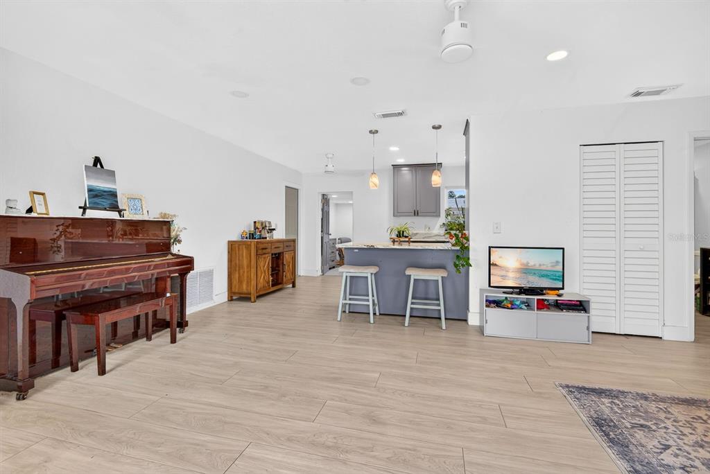 A living room features light wood-look flooring, a piano, and an open kitchen with bar seating — 707 65TH AVENUE DRIVE W, BRADENTON, FL