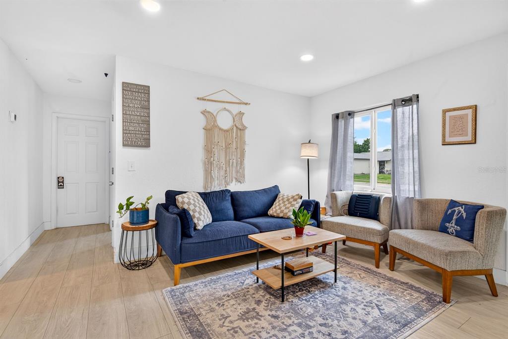 A living room features a blue sofa, two armchairs, a coffee table, and wood-look flooring — 707 65TH AVENUE DRIVE W, BRADENTON, FL