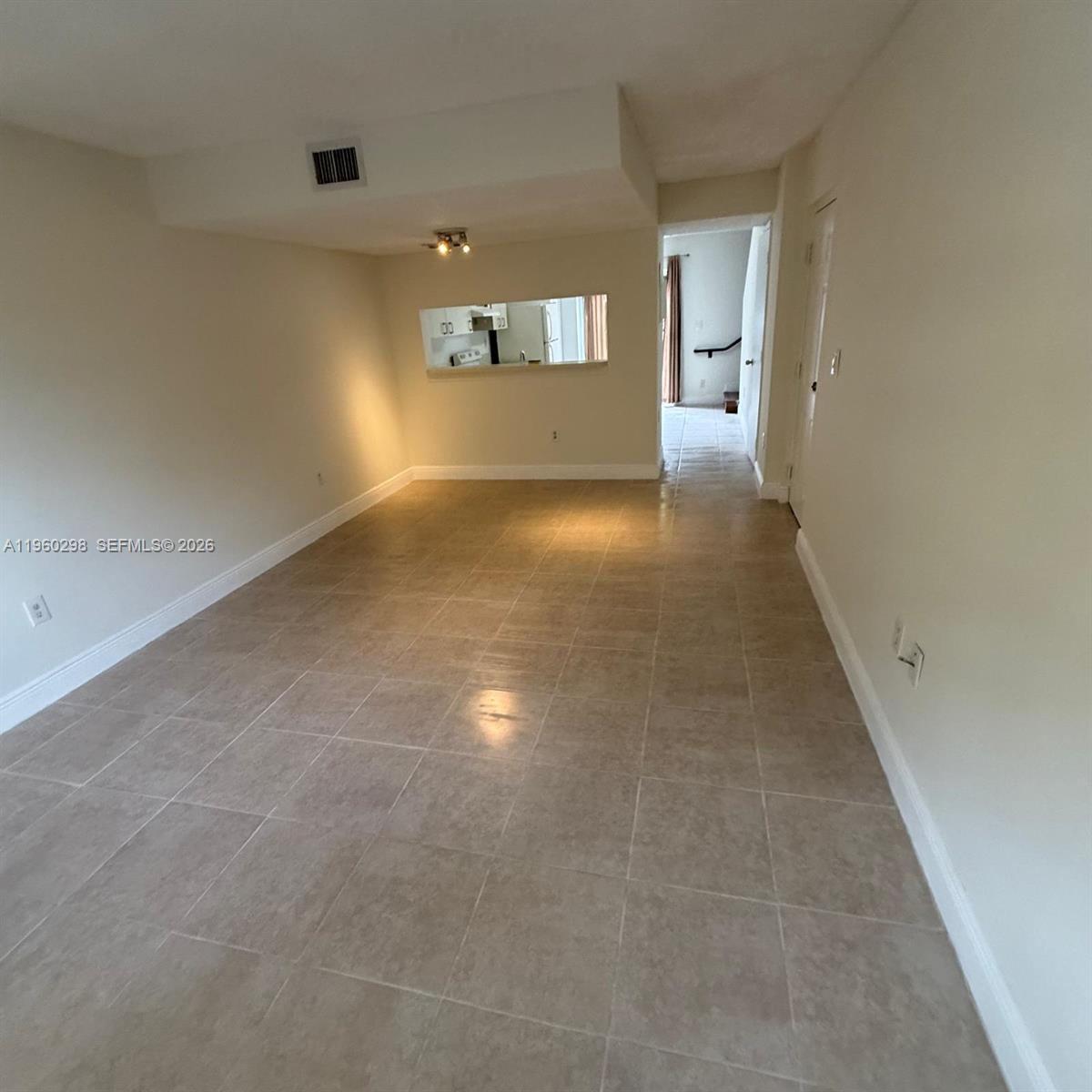 An empty room features beige tile flooring, white walls, and a pass-through window to the kitchen — 8260 SW 149th Ct # 205, Miami FL 33193, MIAMI, FL