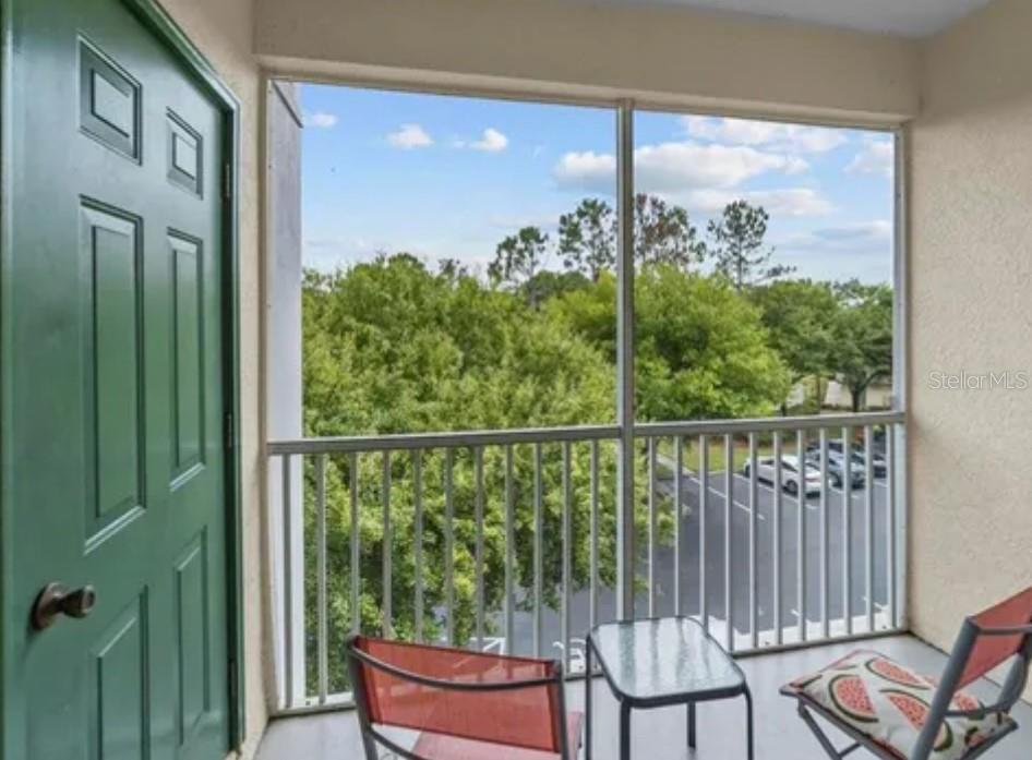 A screened-in balcony features a green door, metal railing, and a view of trees — 8921 LEGACY COURT UNIT 305, KISSIMMEE, FL