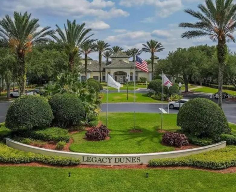 A landscaped entrance sign for Legacy Dunes features palm trees, flags, and a clubhouse building — 8921 LEGACY COURT UNIT 305, KISSIMMEE, FL