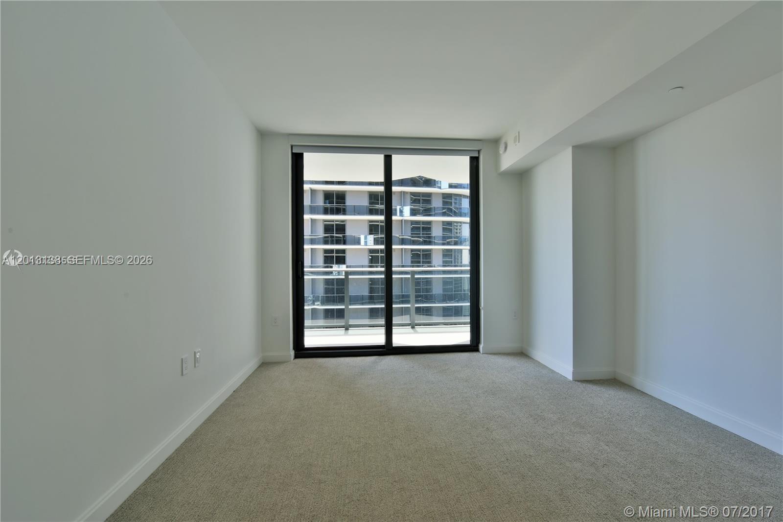 An empty room with beige carpet, white walls, and a sliding glass door to a balcony — 45 SW 9 st # 1907, Miami FL 33130, MIAMI, FL