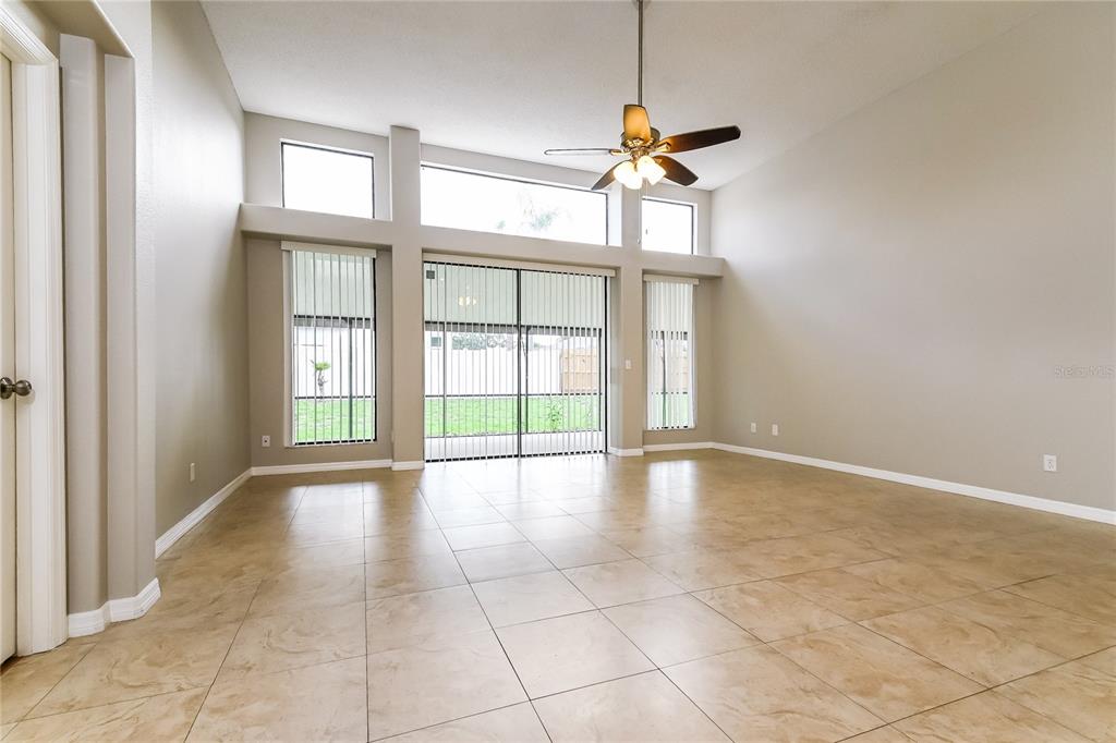 A spacious living room features light-colored tile flooring, vaulted ceilings, and large windows with blinds — 1914 CITRUS ORCHARD WAY, VALRICO, FL