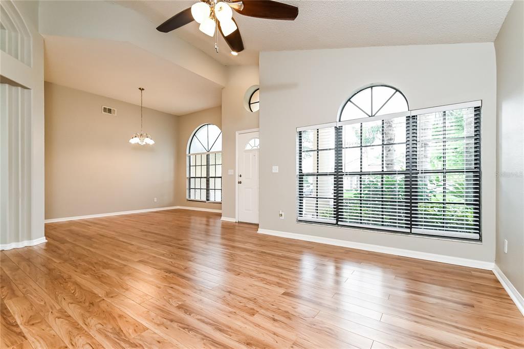 A bright living room features light wood flooring, high ceilings, and large arched windows — 1914 CITRUS ORCHARD WAY, VALRICO, FL