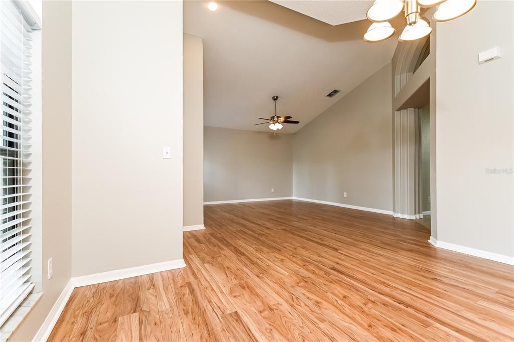 An empty room features light-colored walls, wood-look flooring, a ceiling fan, and a chandelier — 1914 CITRUS ORCHARD WAY, VALRICO, FL