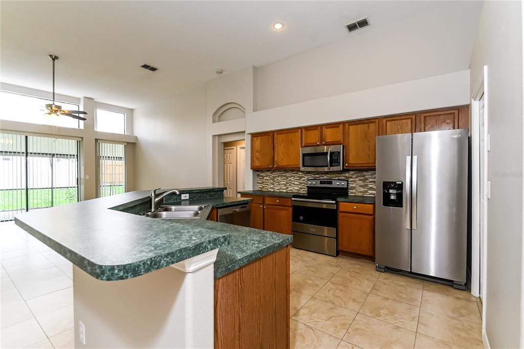 A kitchen features wood cabinets, green laminate countertops, stainless steel appliances, and tile flooring — 1914 CITRUS ORCHARD WAY, VALRICO, FL