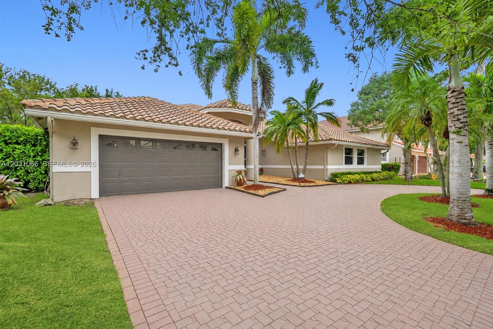 The exterior of a beige house features a tiled roof, a paved driveway, and palm trees — 1776 W Eagle Trace Blvd W, Coral Springs FL 33071, CORAL SPRINGS, FL