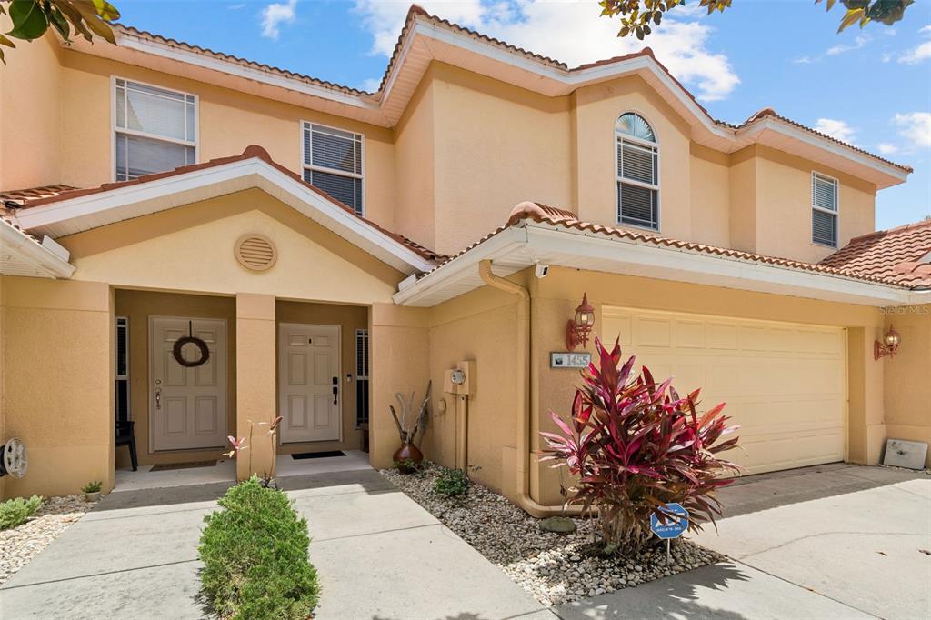 The exterior of a two-story tan townhouse features a two-car garage and two front doors — 1455 HIDDEN COURT, TARPON SPRINGS, FL