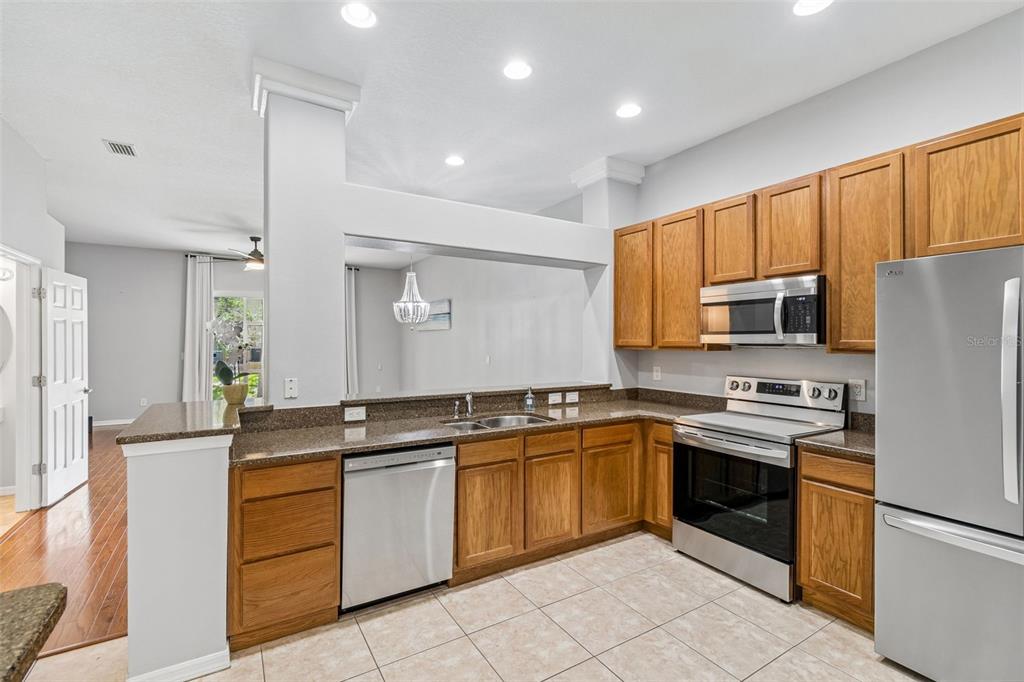 A kitchen features oak cabinets, stainless steel appliances, granite countertops, and tile flooring — 1455 HIDDEN COURT, TARPON SPRINGS, FL