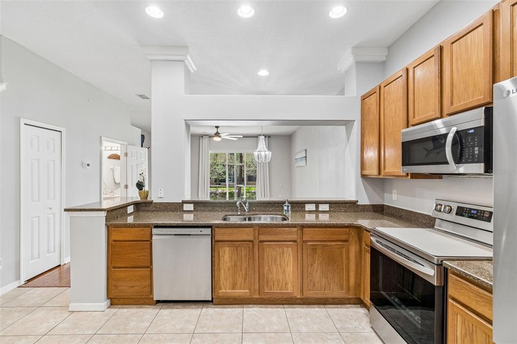 A kitchen with oak cabinets, granite countertops, stainless steel appliances, and a pass-through window — 1455 HIDDEN COURT, TARPON SPRINGS, FL