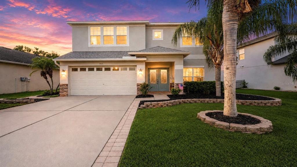 A two-story suburban house features a two-car garage, a palm tree, and a landscaped lawn — 8839 39TH STREET CIRCLE E, PARRISH, FL