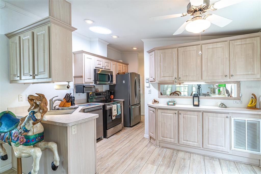 A kitchen features light wood cabinets, stainless steel appliances, and a decorative carousel horse statue — 511 PAR PINES BOULEVARD, DAVENPORT, FL