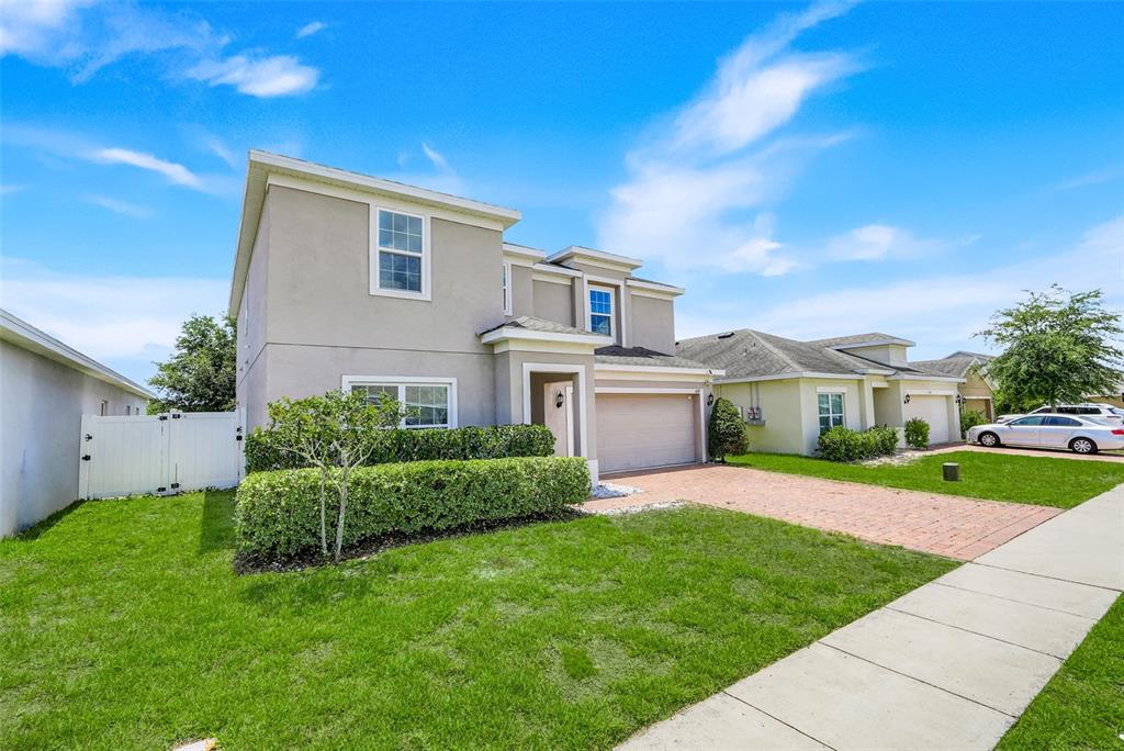 A two-story suburban house with a beige stucco exterior, brick driveway, and manicured hedge — 639 SAMUEL PLACE, DAVENPORT, FL