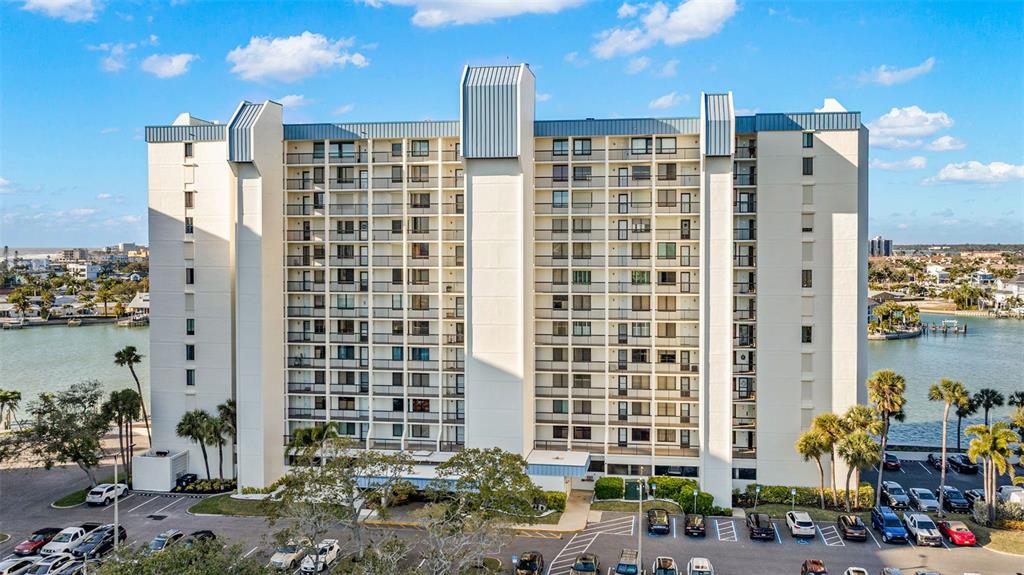A tall, multi-story apartment building stands next to a waterway with a parking lot below — 9495 BLIND PASS ROAD UNIT 204, ST PETE BEACH, FL