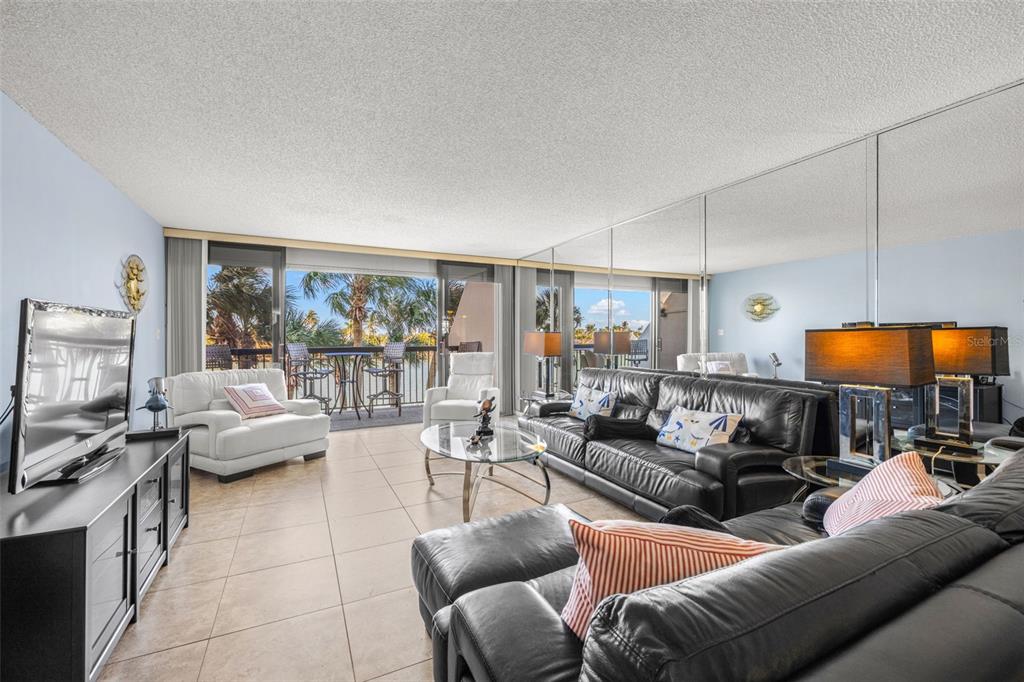 A living room features tile floors, black leather sofas, a glass coffee table, and mirrored walls — 9495 BLIND PASS ROAD UNIT 204, ST PETE BEACH, FL