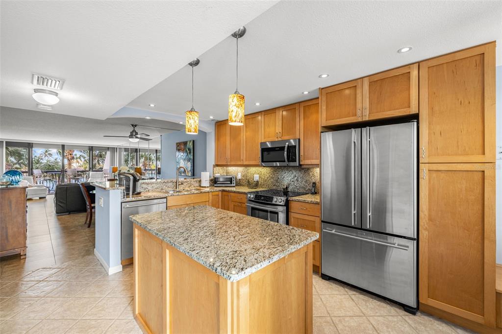 A kitchen features light wood cabinets, granite countertops, stainless steel appliances, and a central island — 9495 BLIND PASS ROAD UNIT 204, ST PETE BEACH, FL