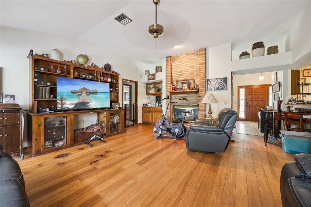 A living room features hardwood floors, a brick fireplace, a large entertainment center, and exercise equipment — 175 WHITE DOVE AVENUE, ORANGE CITY, FL