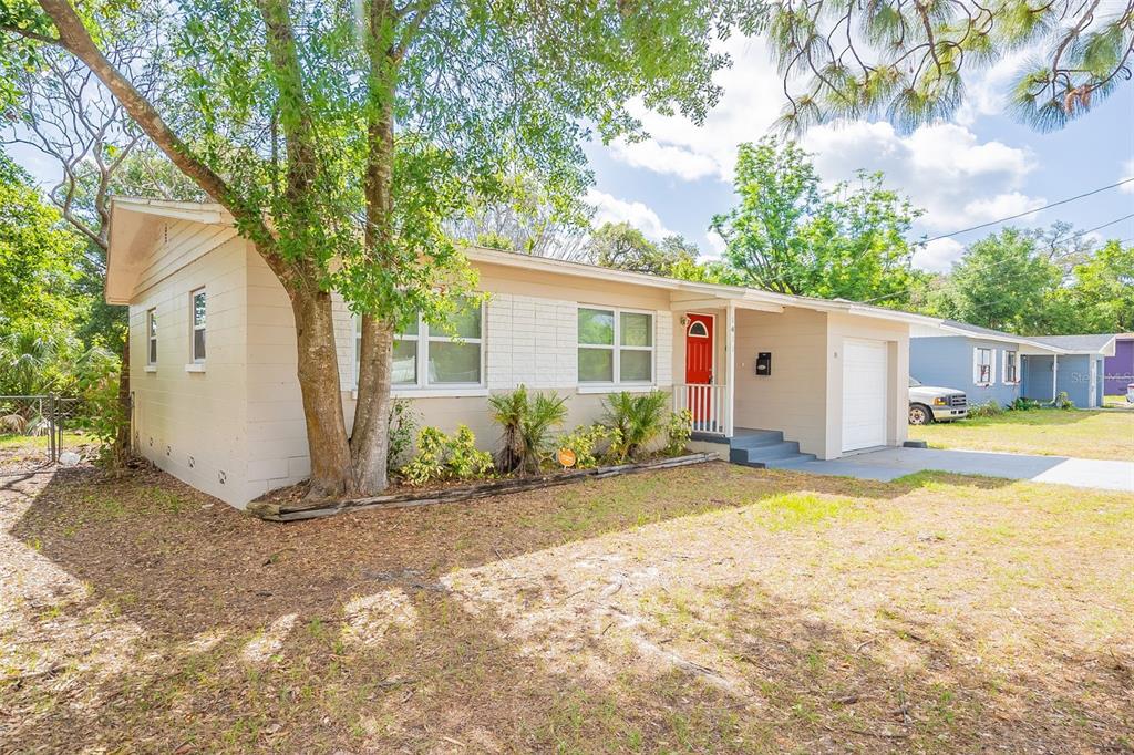 A single-story house with beige siding, a red front door, and a small attached garage — 1411 N POWERS DRIVE, ORLANDO, FL
