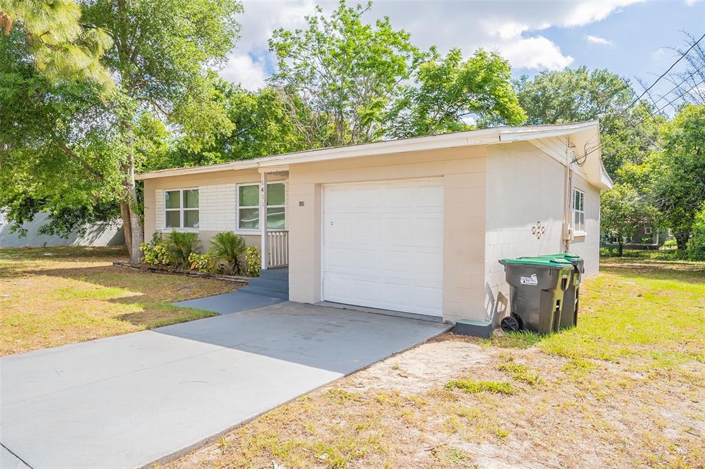 A single-story house with a white garage door, beige siding, and a concrete driveway — 1411 N POWERS DRIVE, ORLANDO, FL