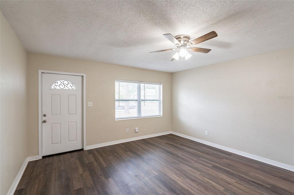 An empty room with light-colored walls, wood-look flooring, a ceiling fan, and a front door — 1411 N POWERS DRIVE, ORLANDO, FL
