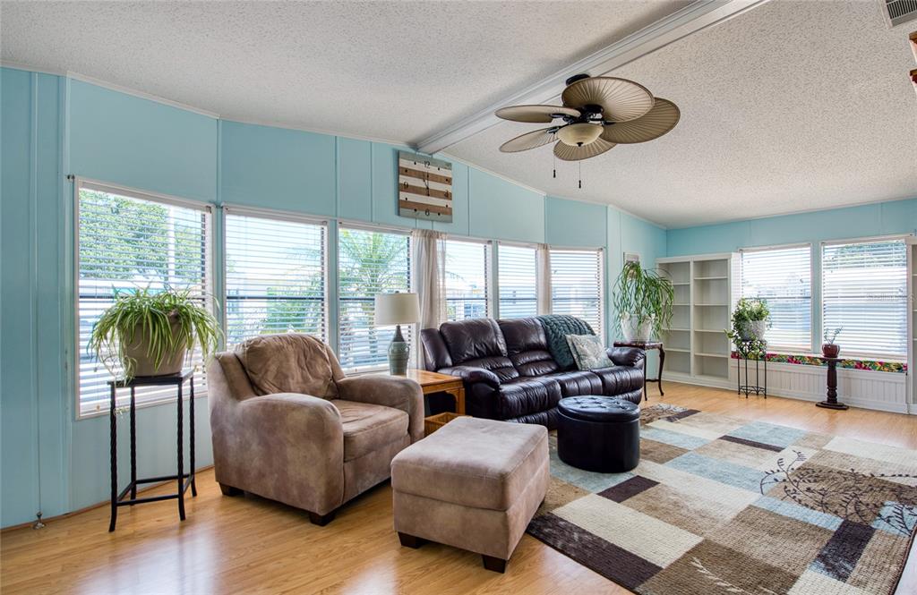 A living room features light blue walls, wood-look flooring, a ceiling fan, and large windows — 228 TARPON LANE, OLDSMAR, FL