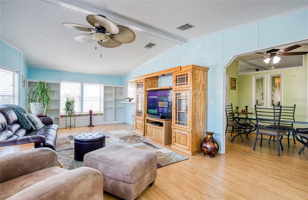 A living room with light blue walls, wood-look flooring, a large entertainment center, and ceiling fans — 228 TARPON LANE, OLDSMAR, FL