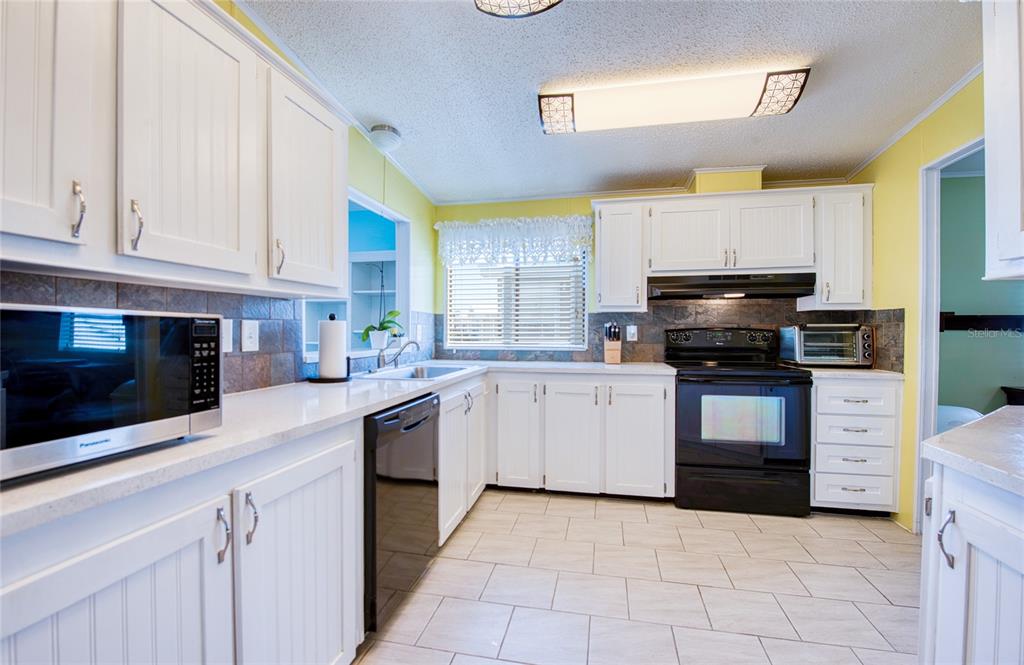 A kitchen features white cabinets, black appliances, tile flooring, and yellow walls — 228 TARPON LANE, OLDSMAR, FL