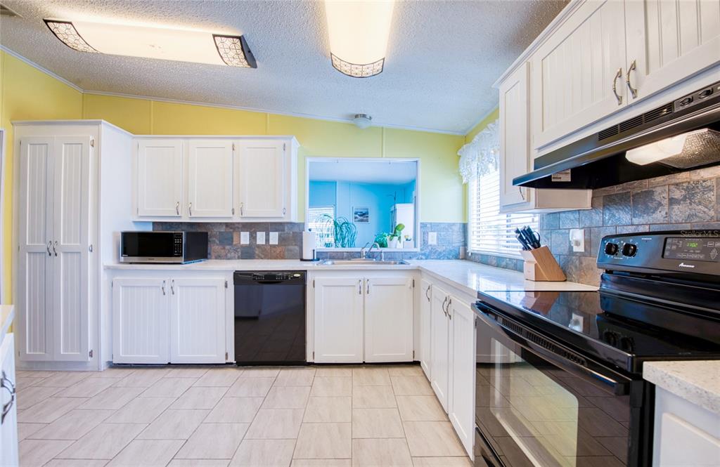 A kitchen with white cabinets, black appliances, tile backsplash, and yellow walls — 228 TARPON LANE, OLDSMAR, FL
