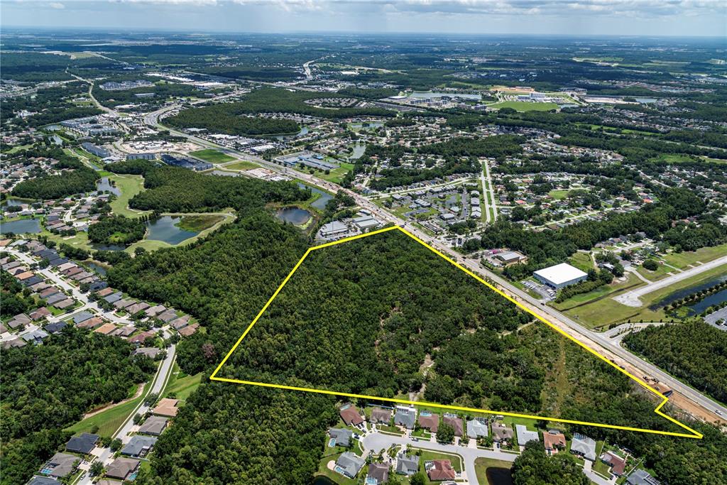 An aerial view shows a large, triangular, wooded plot of land outlined in yellow — N/A N/A, LAND O LAKES, FL