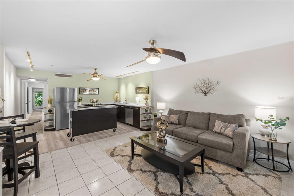 An open-concept living room and kitchen featuring a grey sofa, kitchen island, and tiled floors — 426 32ND AVENUE N UNIT 102E, ST PETERSBURG, FL
