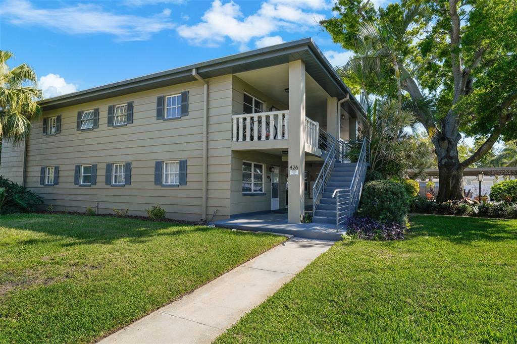 A two-story apartment building with tan siding, a concrete staircase, and a grassy front yard — 426 32ND AVENUE N UNIT 102E, ST PETERSBURG, FL