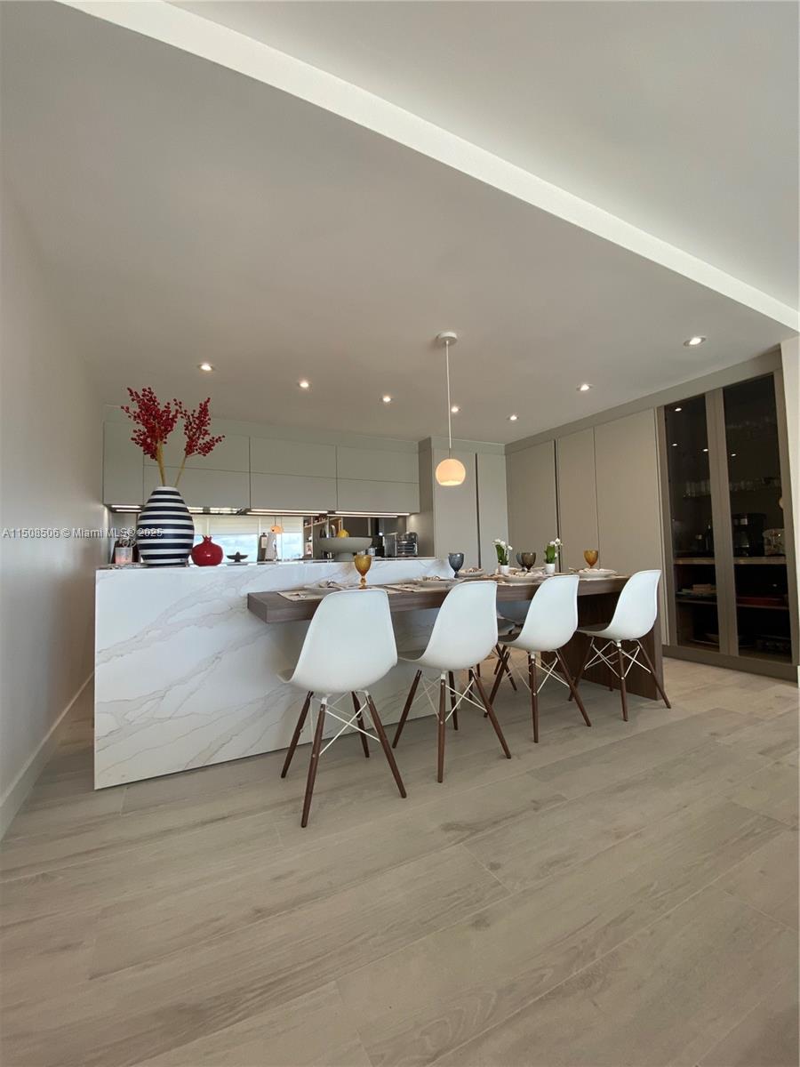 A modern kitchen features a marble-topped island with four white chairs and light wood flooring — 199 Ocean Lane Dr # 1112, Key Biscayne FL 33149, KEY BISCAYNE, FL