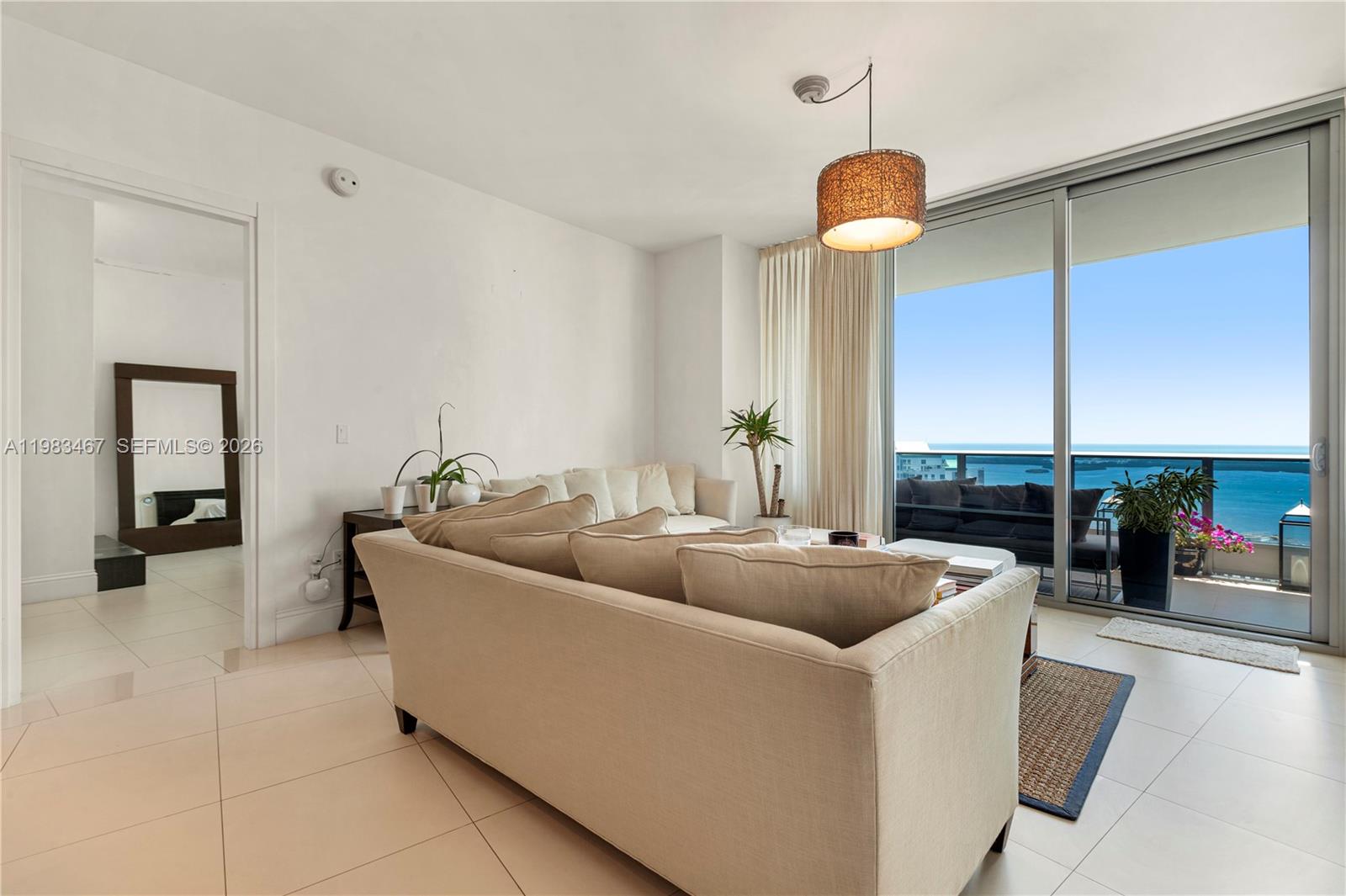 A living room features a beige sofa, tile flooring, and a balcony overlooking the ocean — 200 Biscayne Boulevard Way # 4907, Miami FL 33131, MIAMI, FL