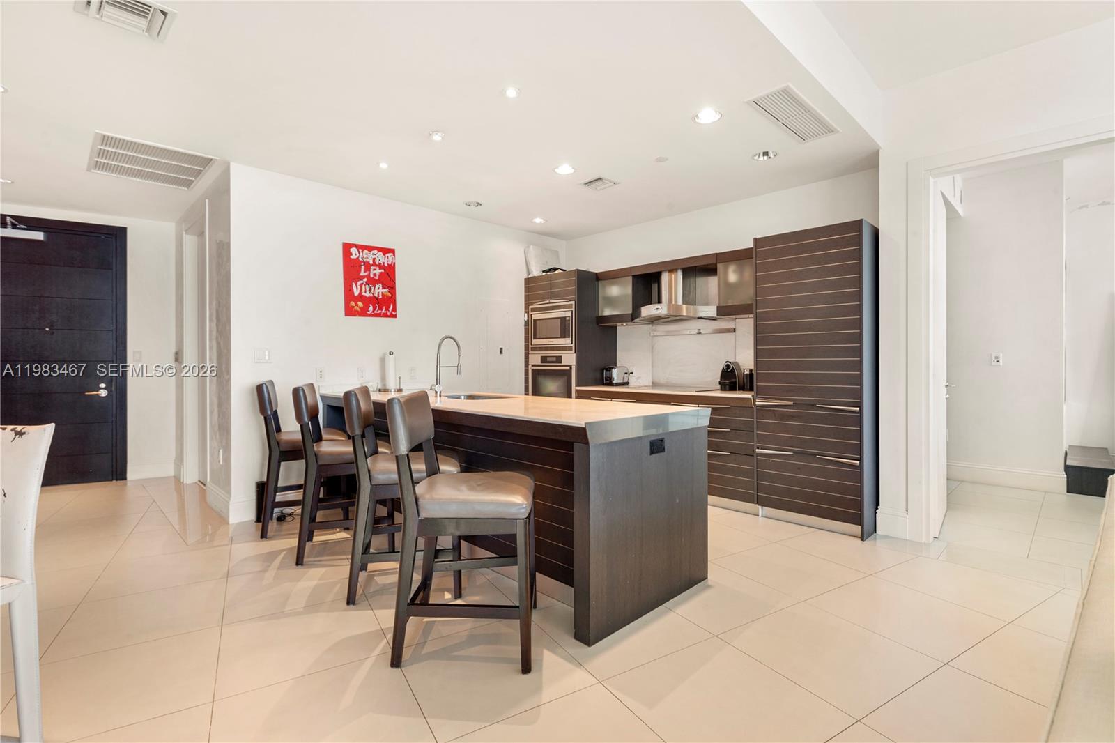 A modern kitchen features dark wood cabinetry, a central island with bar seating, and tile flooring — 200 Biscayne Boulevard Way # 4907, Miami FL 33131, MIAMI, FL