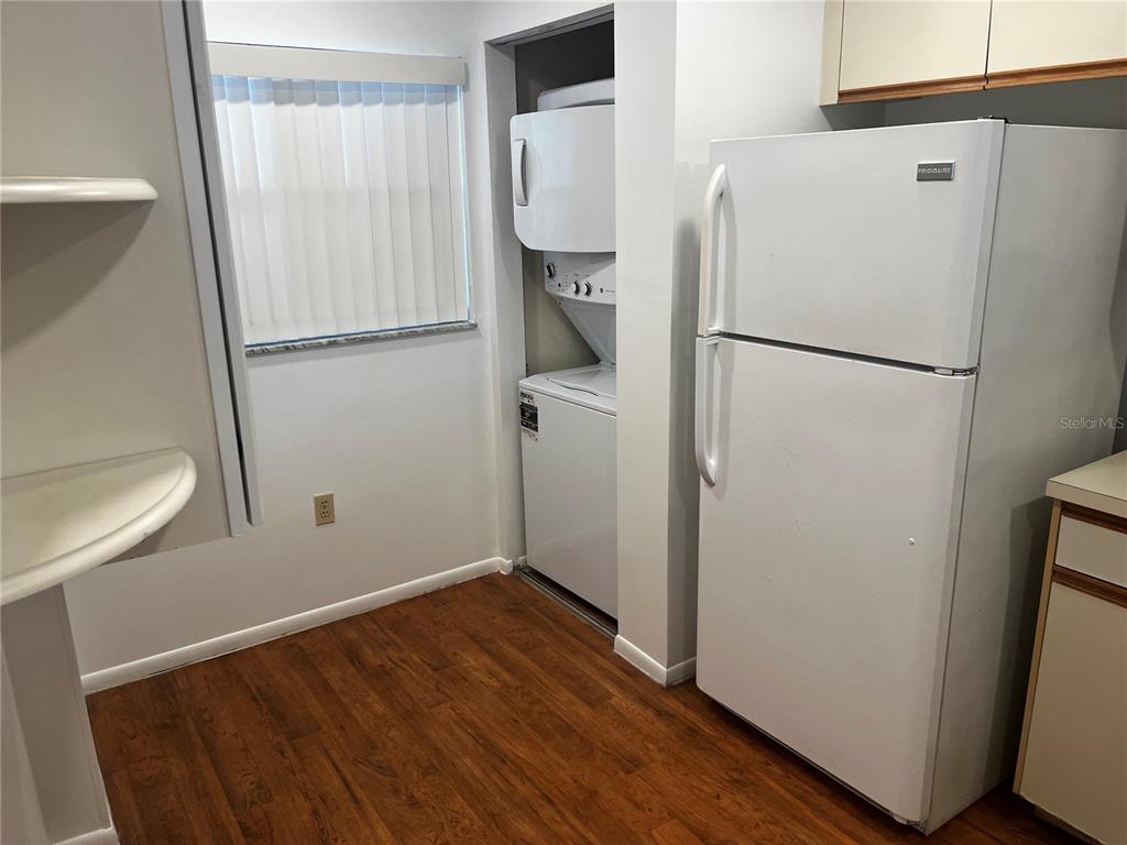 A kitchen area features wood-look flooring, a white refrigerator, and a stacked washer and dryer — 800 COVE CAY DRIVE UNIT 3F, CLEARWATER, FL