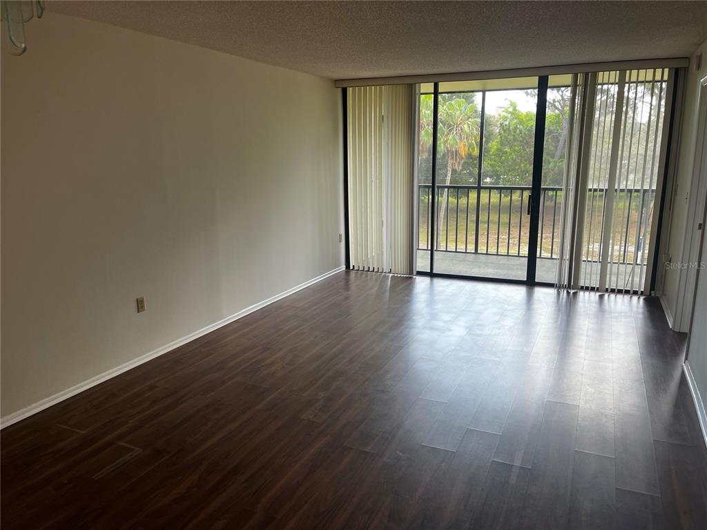 An empty room with dark wood-look flooring and a sliding glass door leading to a balcony — 800 COVE CAY DRIVE UNIT 3F, CLEARWATER, FL