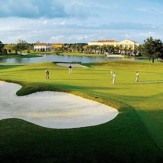 A golf course green features a sand bunker, several golfers, and a lake with buildings — 235 ANASTASIA DRIVE, POINCIANA, FL