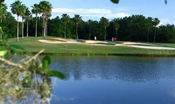 A golf course green with sand bunkers and palm trees sits behind a large pond — 235 ANASTASIA DRIVE, POINCIANA, FL