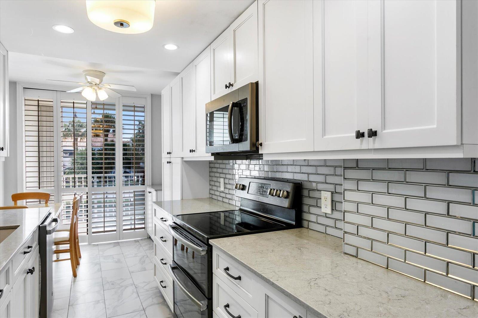 A white kitchen features gray subway tile backsplash, quartz countertops, and a black range — 2860 S Ocean Boulevard # 214, Palm Beach FL 33480, PALM BEACH, FL