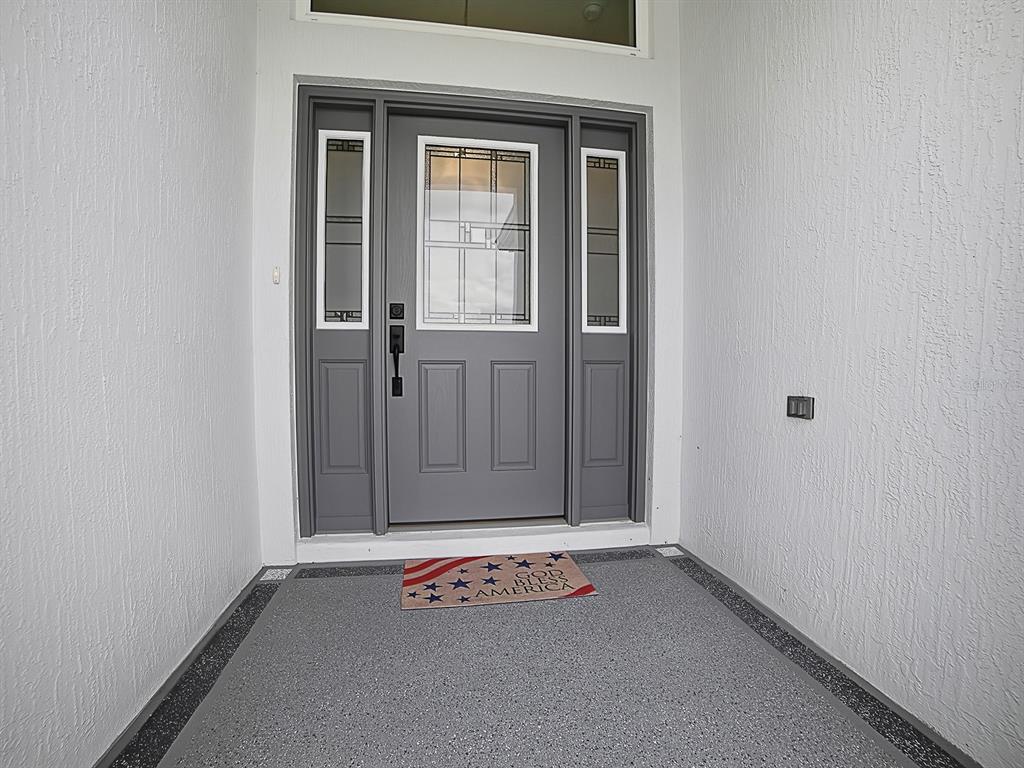 A gray front door with sidelights and a decorative glass insert sits under a transom window — 1404 HEARNS LOOP, THE VILLAGES, FL