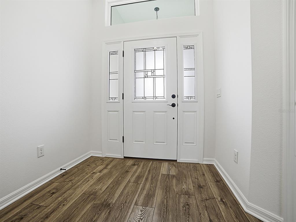 An entryway features a white front door with sidelights, a transom window, and wood-look flooring — 1404 HEARNS LOOP, THE VILLAGES, FL