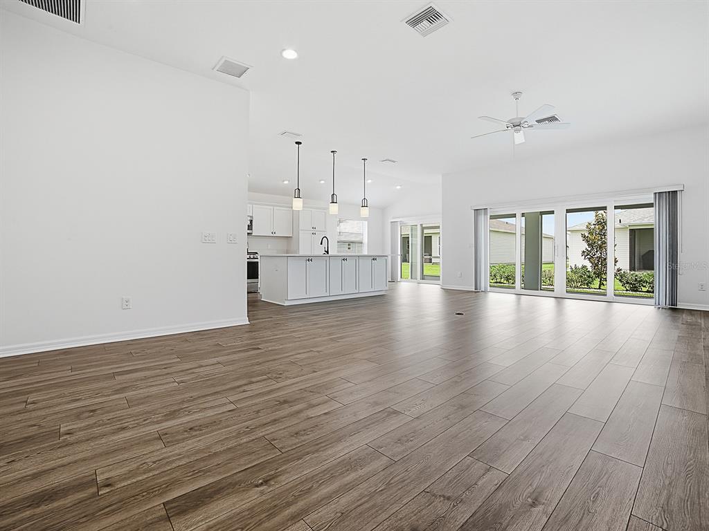 An open-concept living area features wood-look flooring, white walls, and a kitchen with an island — 1404 HEARNS LOOP, THE VILLAGES, FL