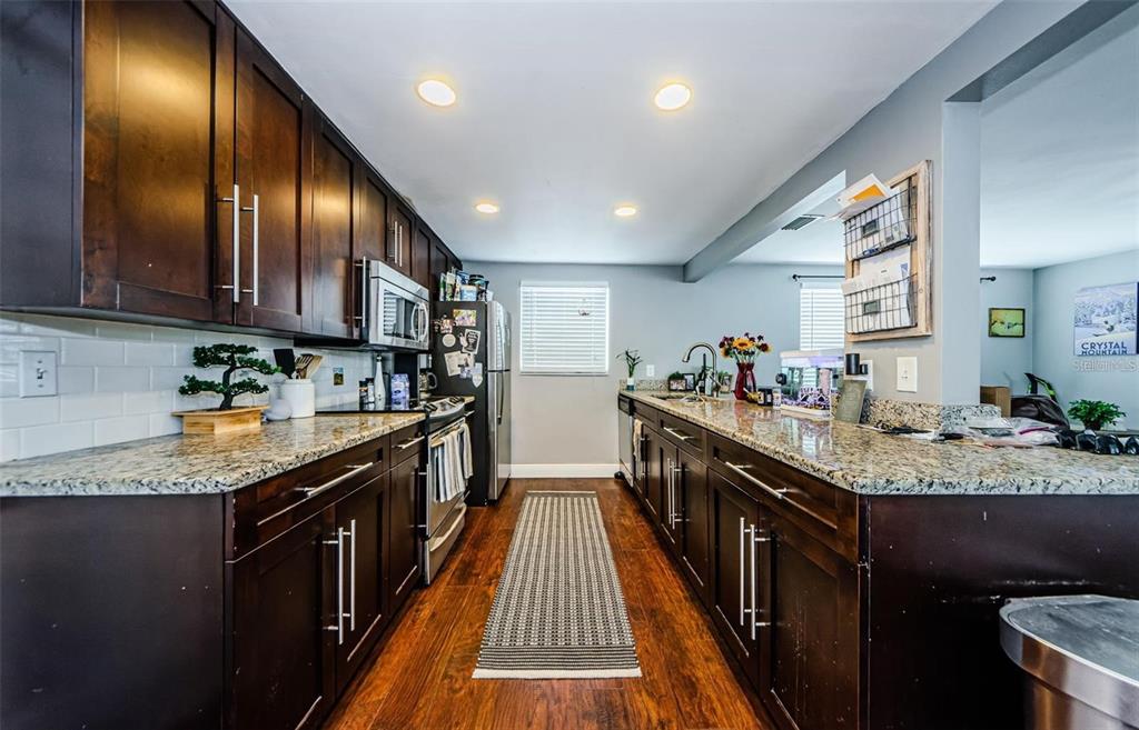 A kitchen features dark wood cabinets, granite countertops, stainless steel appliances, and wood-look flooring — 5915 OTIS DRIVE, NEW PORT RICHEY, FL