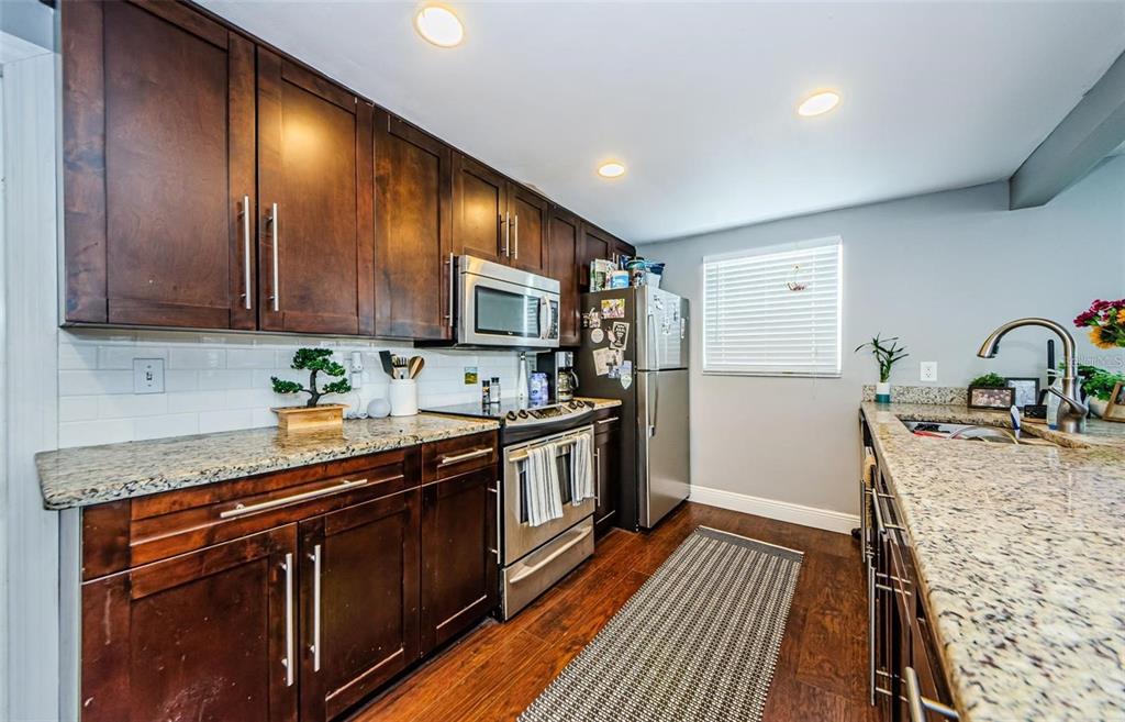 A kitchen features dark wood cabinets, granite countertops, stainless steel appliances, and a tile backsplash — 5915 OTIS DRIVE, NEW PORT RICHEY, FL