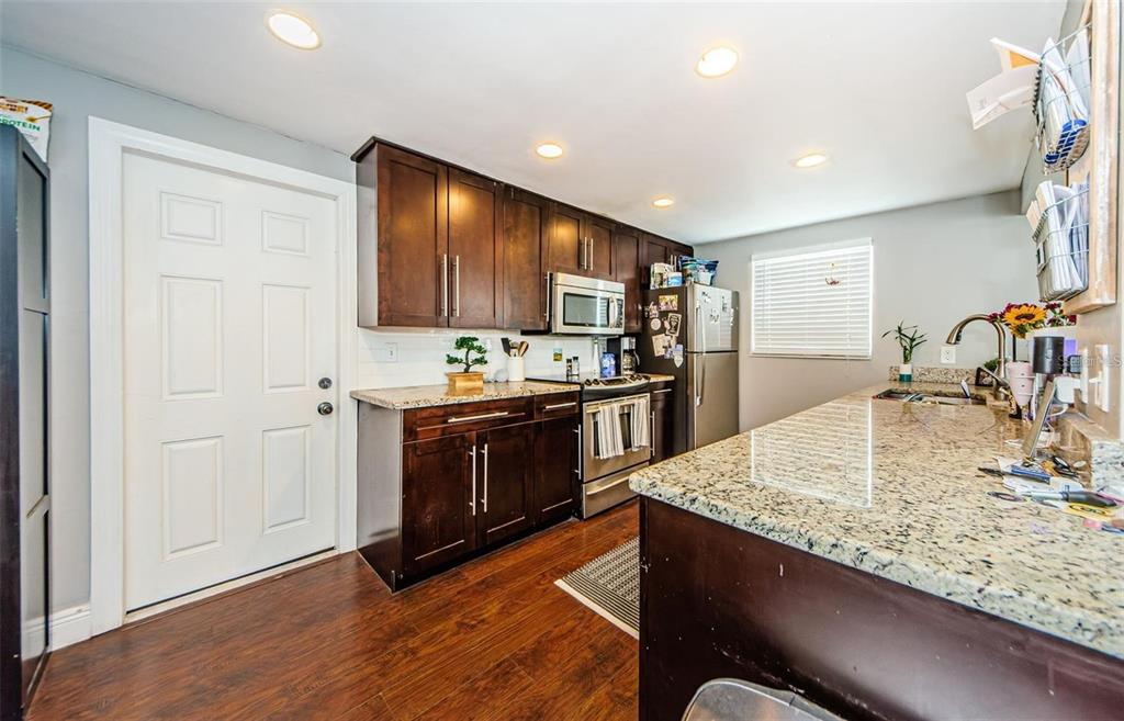 A kitchen features dark wood cabinets, granite countertops, stainless steel appliances, and wood-look flooring — 5915 OTIS DRIVE, NEW PORT RICHEY, FL