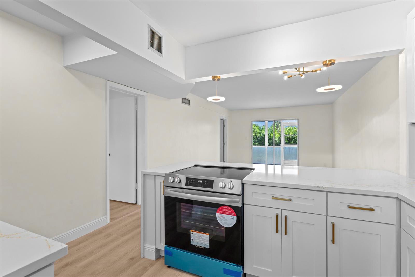 A kitchen with white cabinets, a new electric range, and quartz countertops overlooks a living area — 2647 Garden Drive # 101, Lake Worth FL 33461, LAKE WORTH, FL