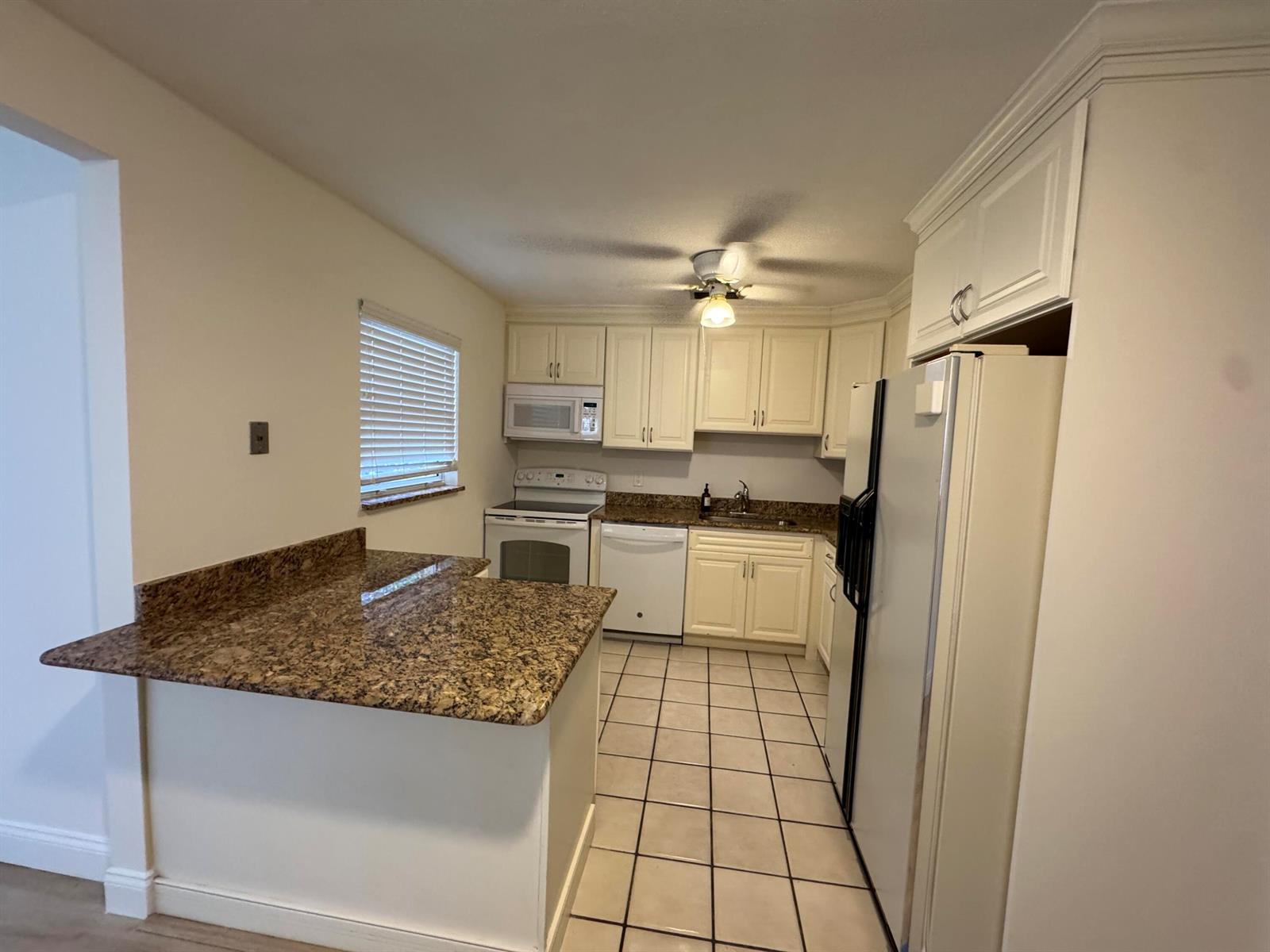 A kitchen features white cabinets, granite countertops, white appliances, and tiled flooring — 4353 Broadway Street, Lake Worth FL 33461, LAKE WORTH, FL