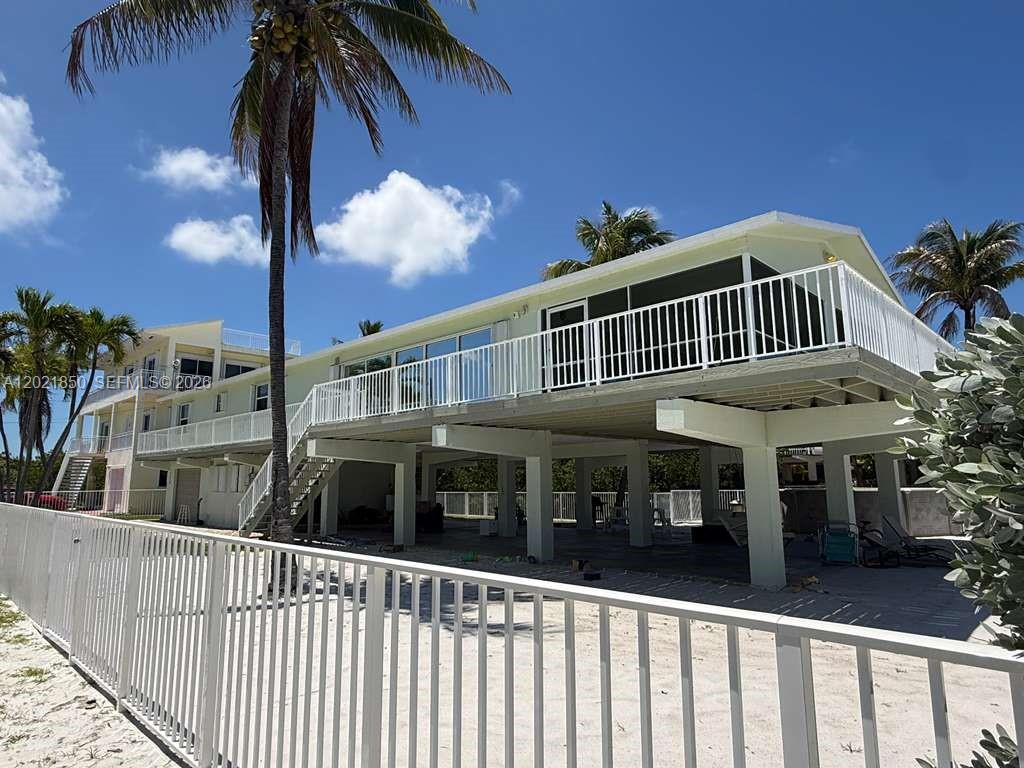 An elevated house with a white railing and a staircase stands on a sandy lot — 172 Valois Blvd, Key Largo FL 33037, KEY LARGO, FL