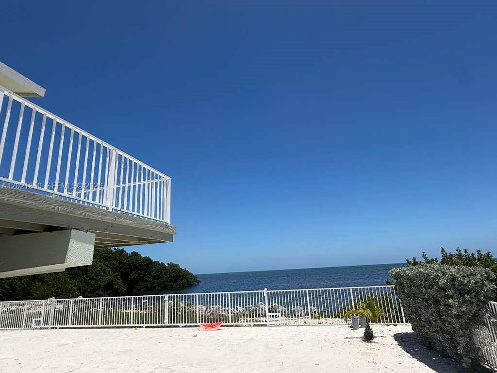 A white balcony overlooks a sandy patio, a white fence, and the ocean — 172 Valois Blvd, Key Largo FL 33037, KEY LARGO, FL