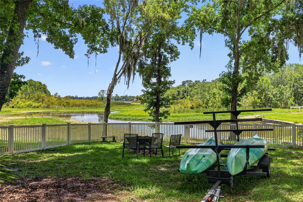 A grassy backyard features a kayak trailer, outdoor chairs, and a white fence overlooking water — 11932 SE 196TH STREET, DUNNELLON, FL